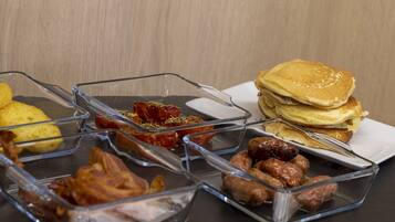 A breakfast buffet with various food items including eggs, bacon, sausages, and pancakes.
