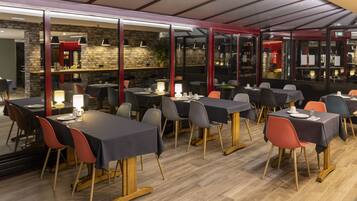 A restaurant with tables and chairs, a brick wall, and a glass partition.