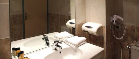 Un baño con lavamanos, espejo, dispensador de toallas y retrete.