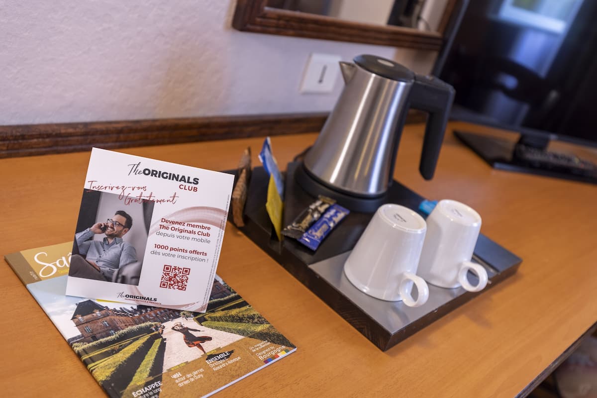 Ein Hotel-Empfangsbereich mit Kaffeemaschine, zwei weißen Tassen, einer Broschüre und einem gerahmten Spiegel.