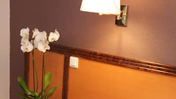 A hotel room with a bed, a nightstand with a potted orchid, and a wall-mounted lamp.