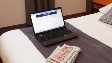 A laptop on a bed with a newspaper and a pillow.
