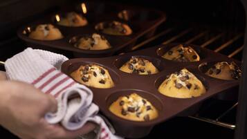 A hand holding a baking tray with muffins inside an oven.