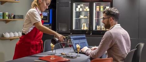 A person pouring wine into glasses at a table with a laptop and a red folder.