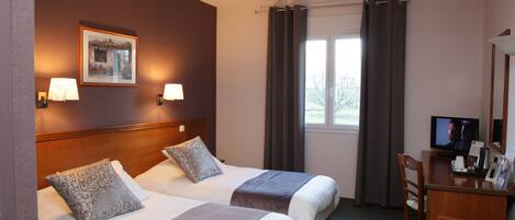 A hotel room with two beds, a desk with a television, and a window with curtains.
