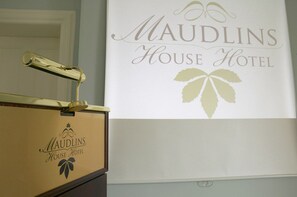 A sign for Maudlins House Hotel with a gold-colored handle on a wooden counter. - Maudlins House Hotel (Naas)