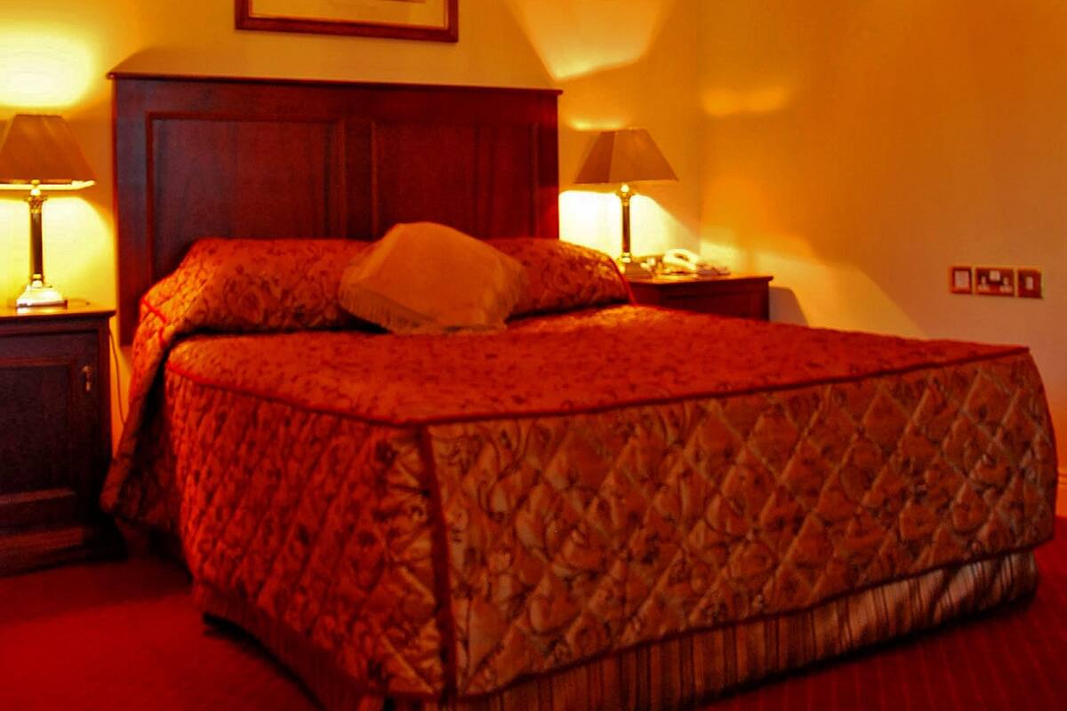 A bedroom with a wooden ceiling, a bed with a patterned bedspread, two bedside lamps, and a framed picture on the wall.
