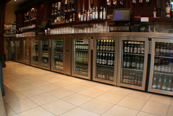 Zona de bar con varias neveras llenas de bebidas y un mostrador con una caja registradora.