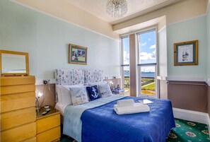 Un dormitorio con una cama grande, un aparador de madera, una mesita de noche, una araña y vistas al mar.