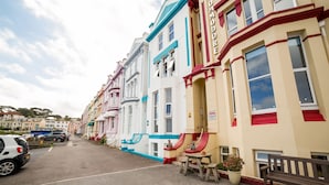 A row of colorful Victorian-style buildings with a red bench and a small table with a potted plant. - The Commodore (Paignton)