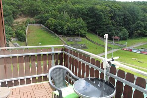A balcony with a view of a sports field, a chair, and a table.