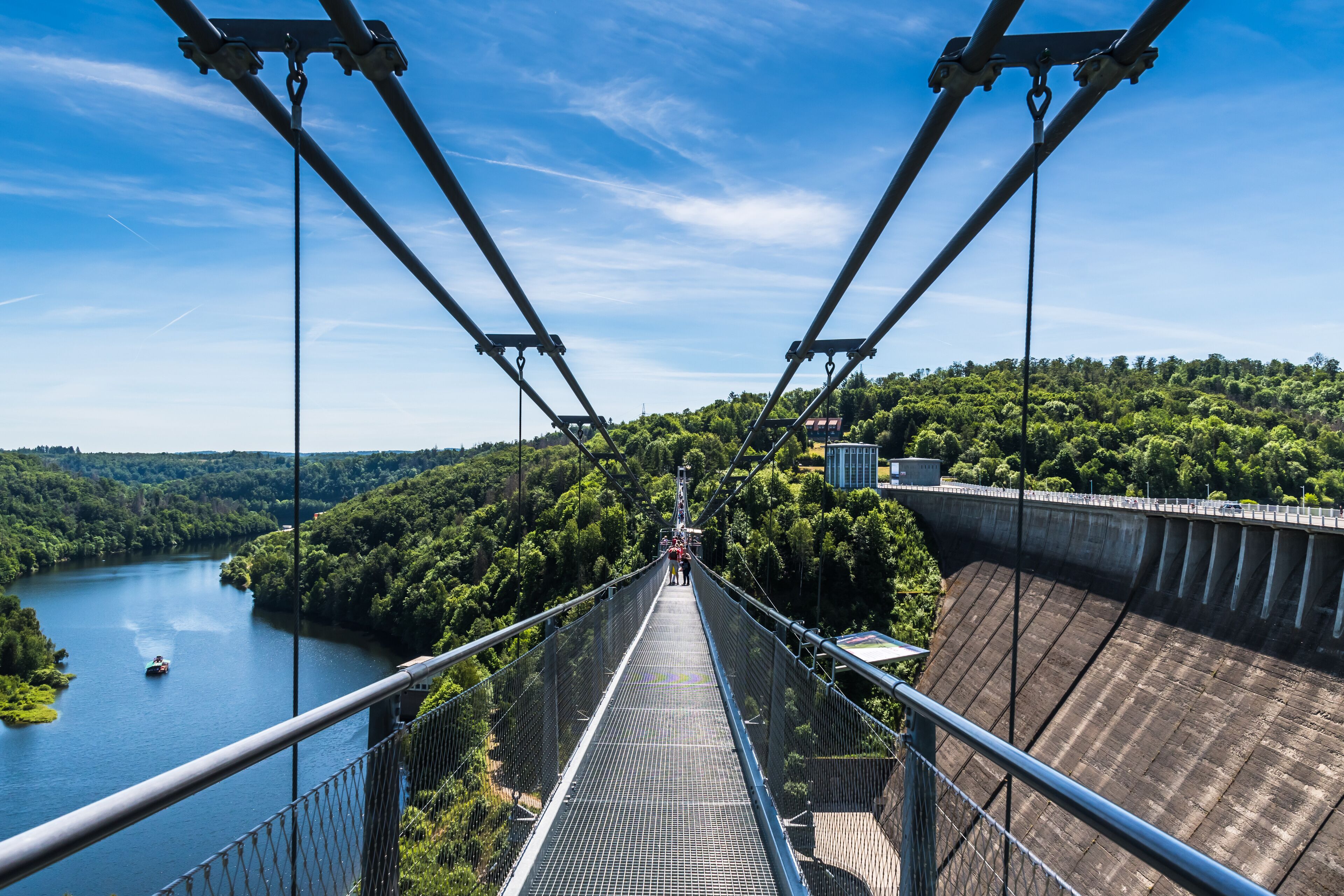 A suspension bridge with a metal walkway, surrounded by lush greenery and a river below.