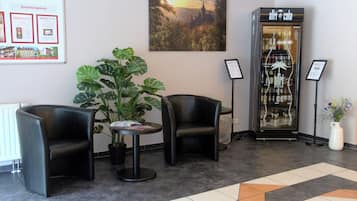 A lobby with two black leather chairs, a potted plant, a glass display case with bottles, and a framed picture on the wall.