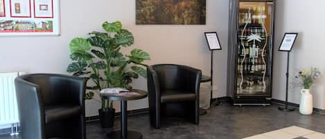 Un hall con dos sillones de cuero negro, una planta en maceta, una vitrina con botellas y un cuadro en la pared.