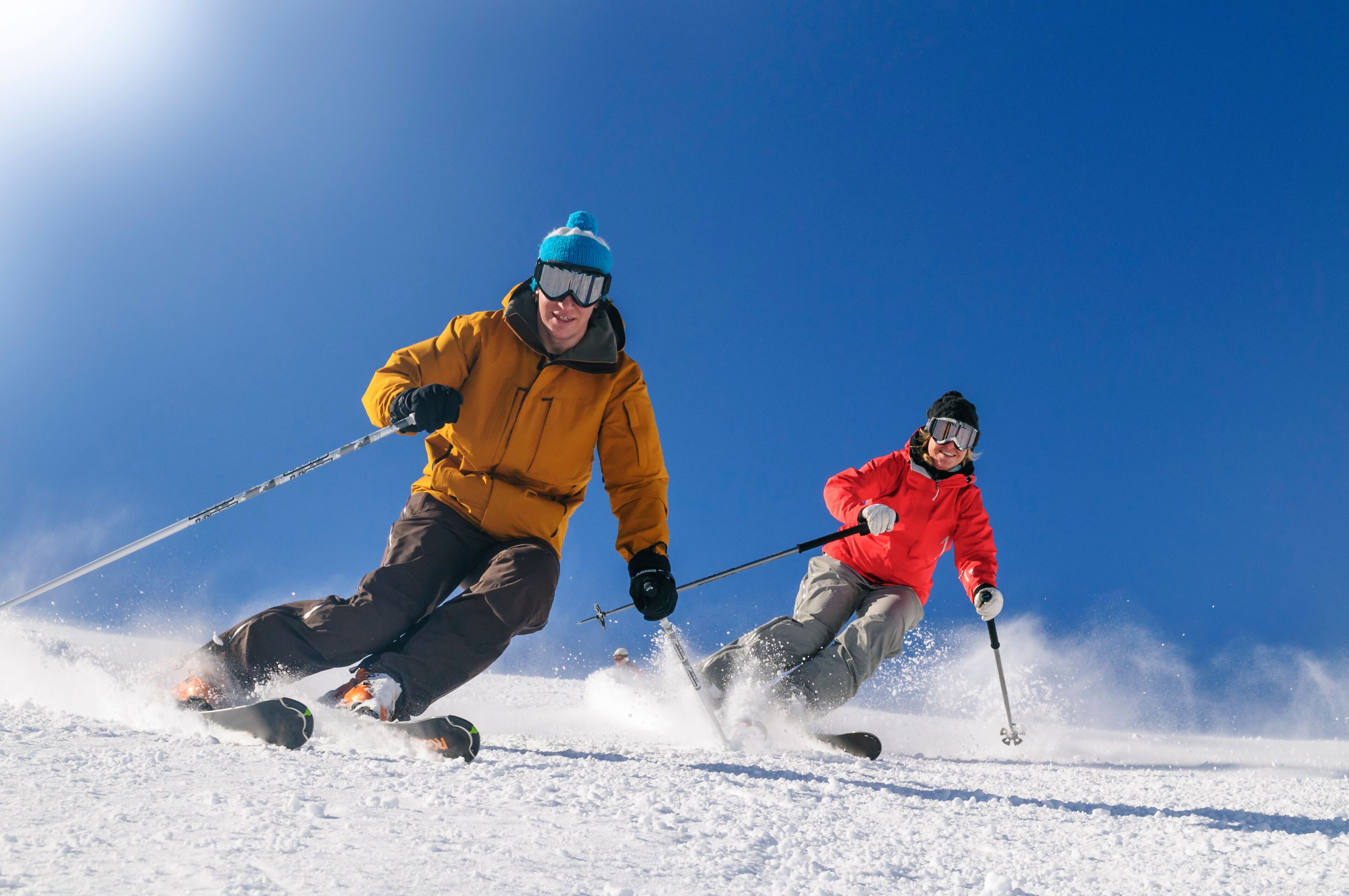 Two people skiing on a snowy slope with clear skies.