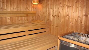 A wooden sauna with benches and a metal container for heating.