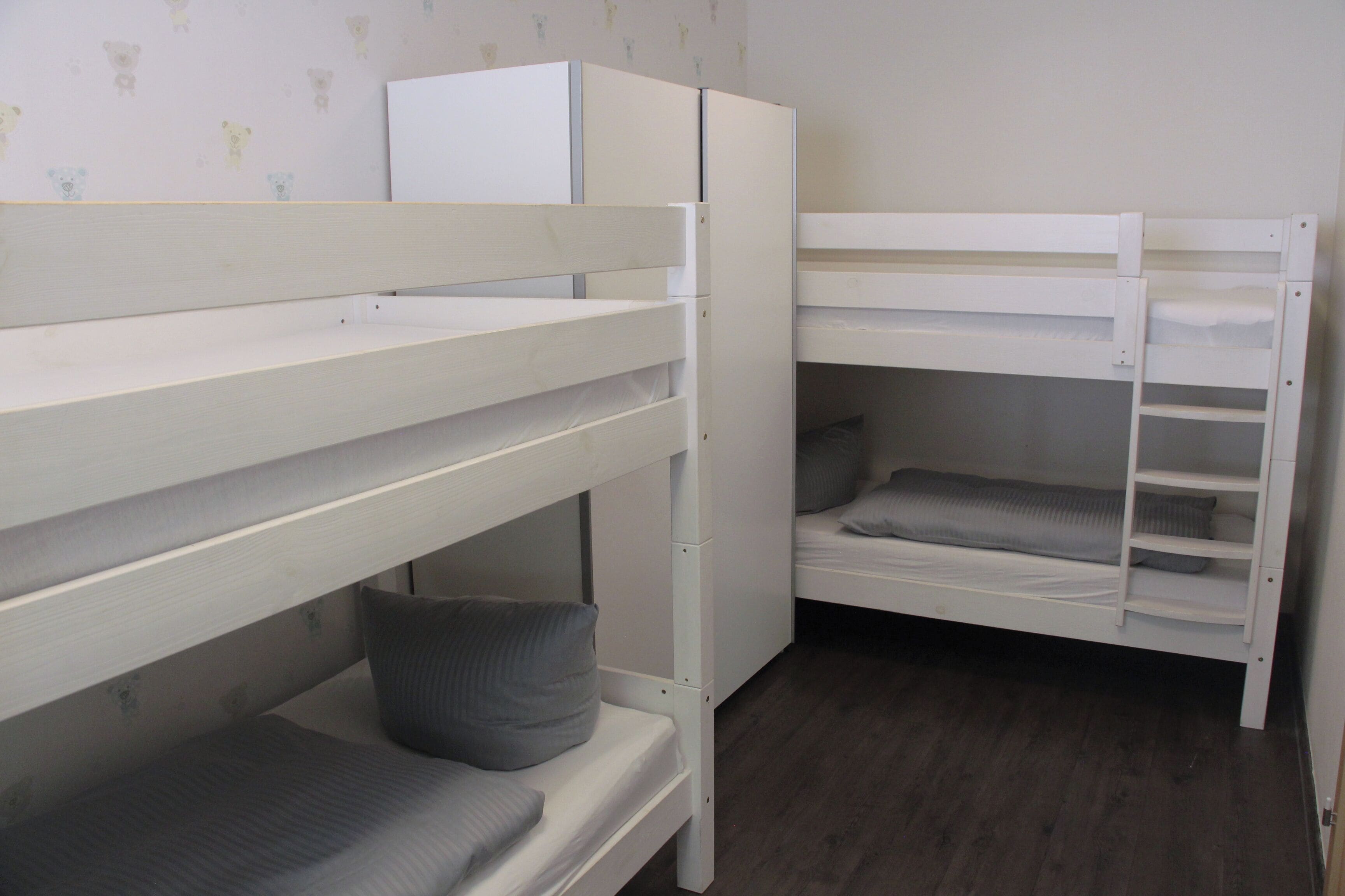 A bunk bed room with a white wardrobe and a grey mattress.