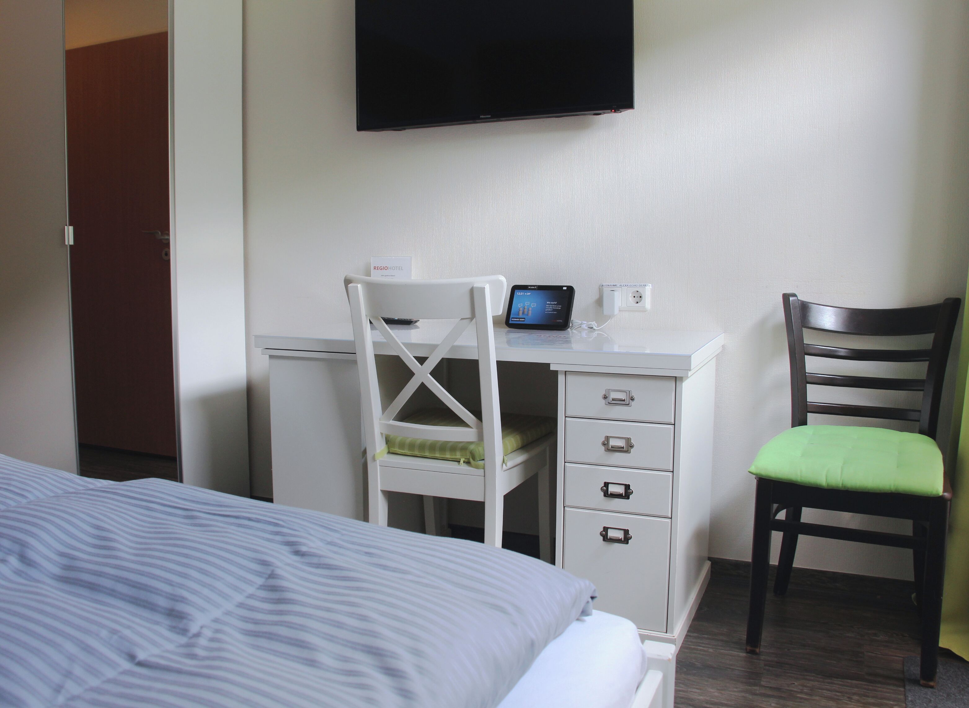 Une chambre d’hôtel équipée d’un lit, d’un bureau avec un ordinateur, d’une chaise et d’un téléviseur fixé au mur.