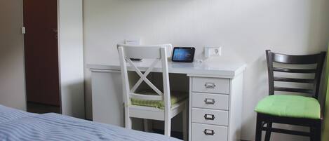 A hotel room with a bed, a desk with a computer, a chair, and a TV mounted on the wall.