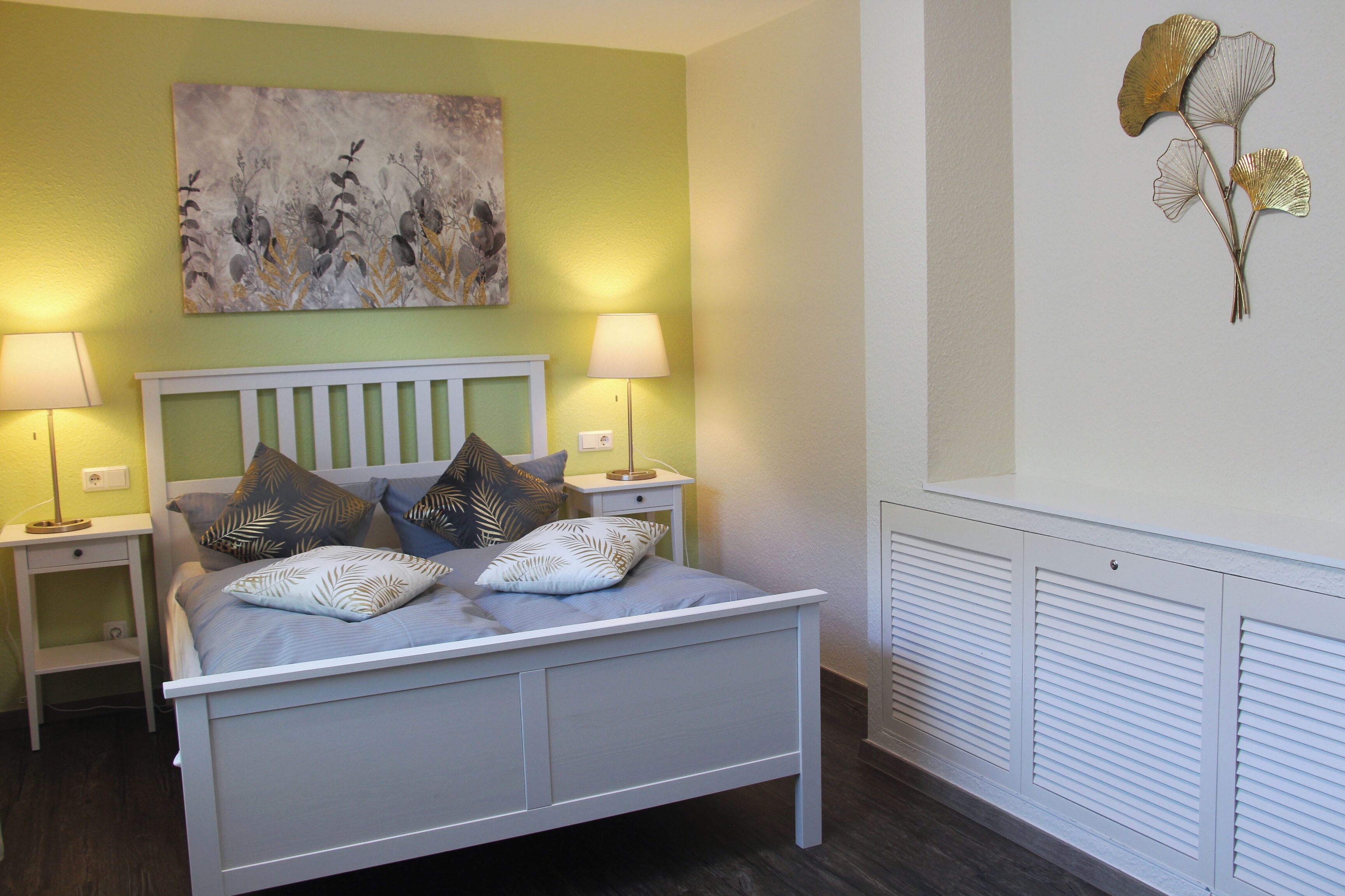A bedroom with a bed, two bedside tables, a wall-mounted lamp, and a radiator.