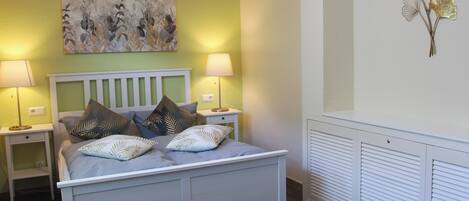 A bedroom with a bed, two bedside tables, a wall-mounted lamp, and a radiator.