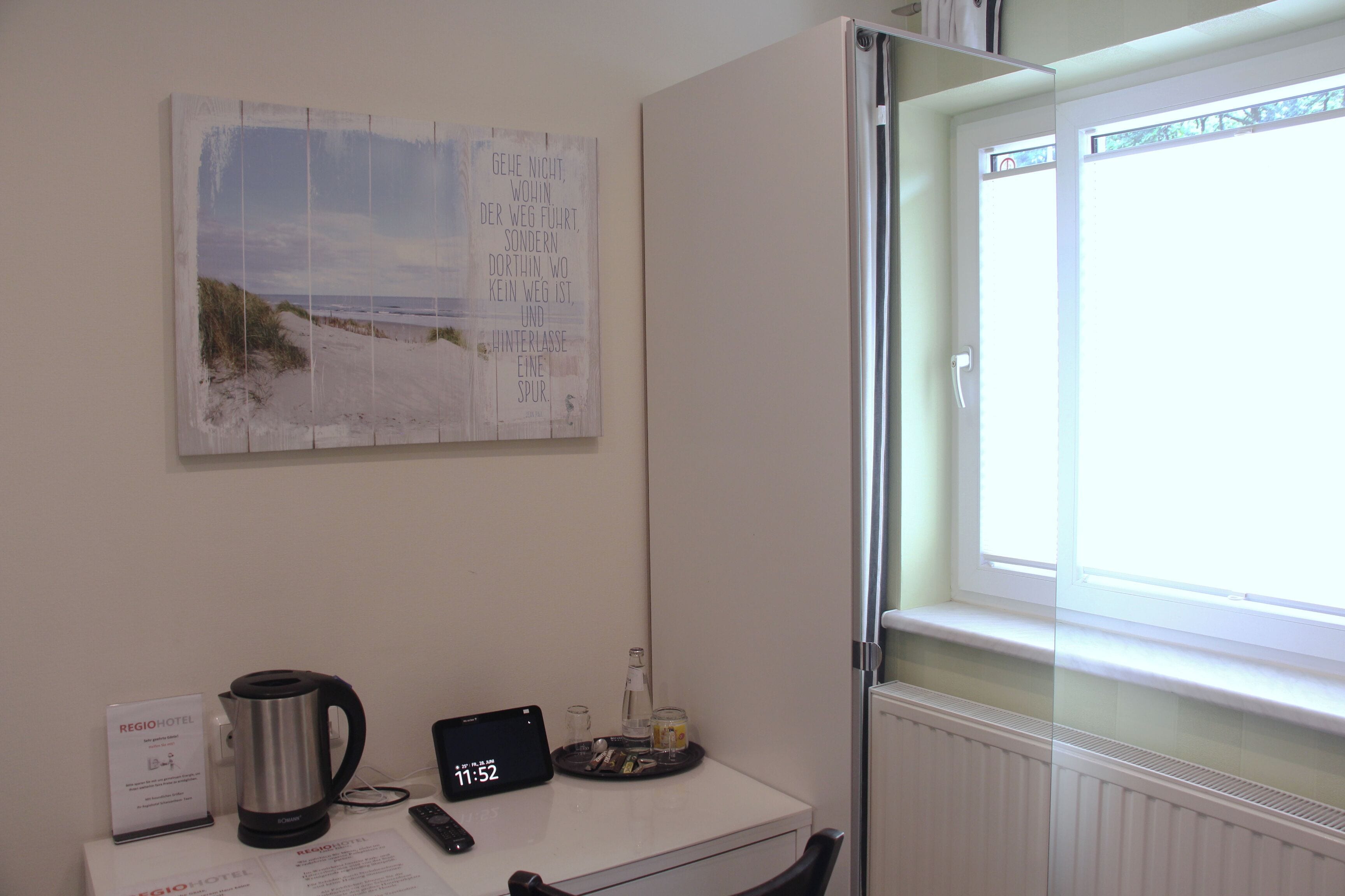 Habitación de hotel con escritorio, cafetera, tableta, control remoto y ventana con vista a la playa.