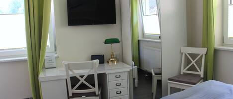 Habitación de hotel con escritorio, una silla, cama, televisor y ventana con cortinas.