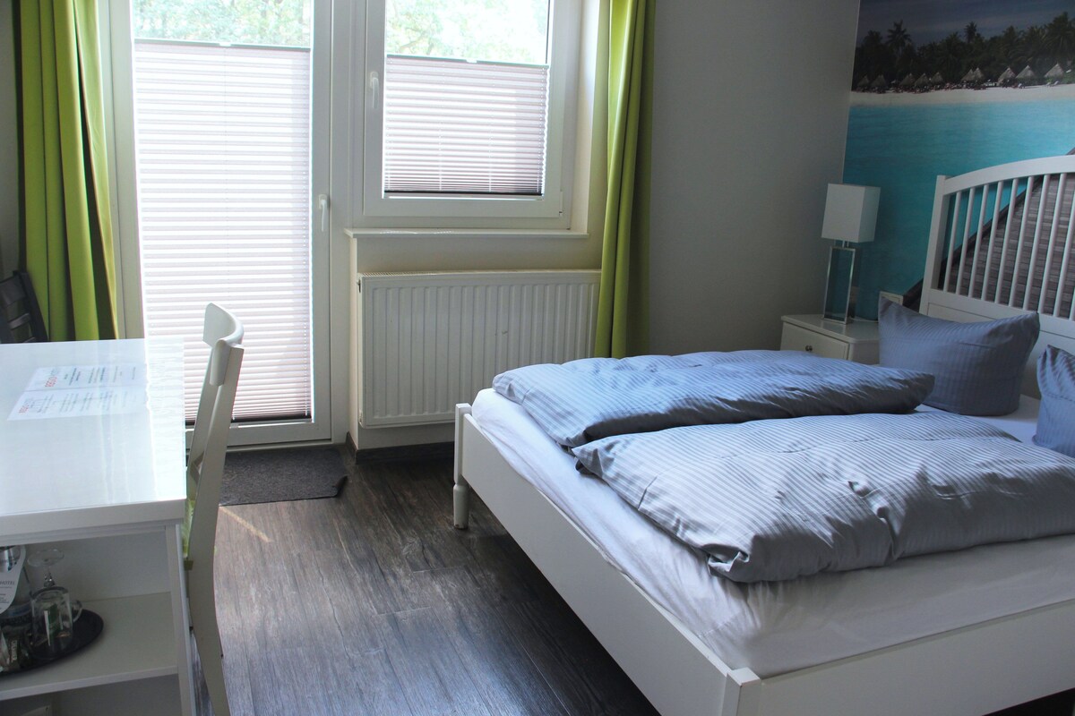 Quarto com cama, escrivaninha e janela com persianas.