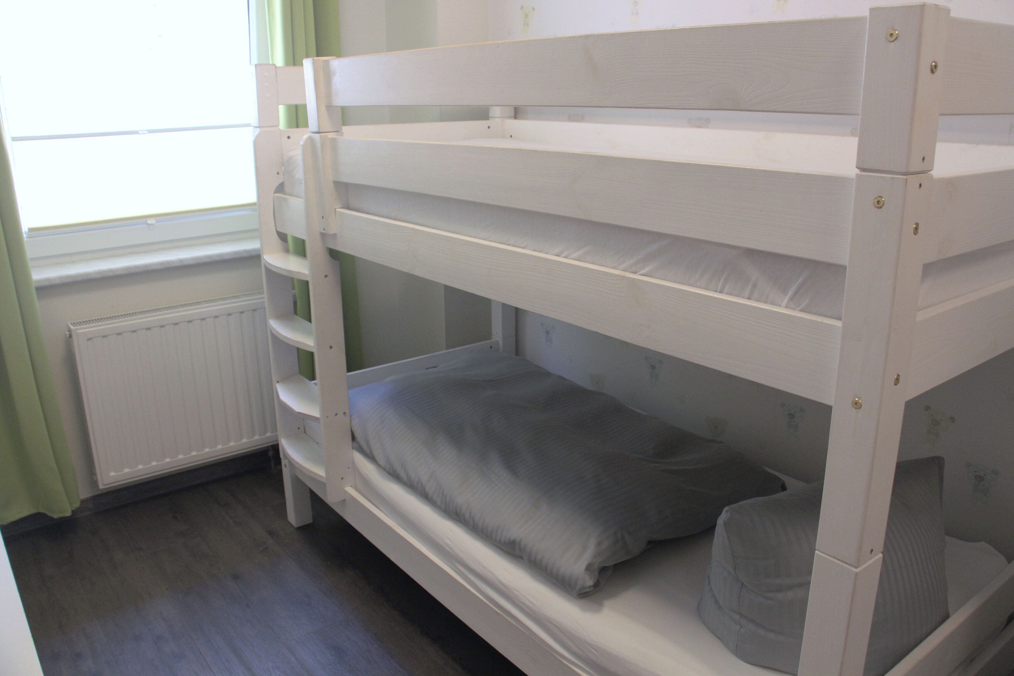 Un lit superposé avec un matelas et des oreillers, un radiateur et une fenêtre avec des rideaux.