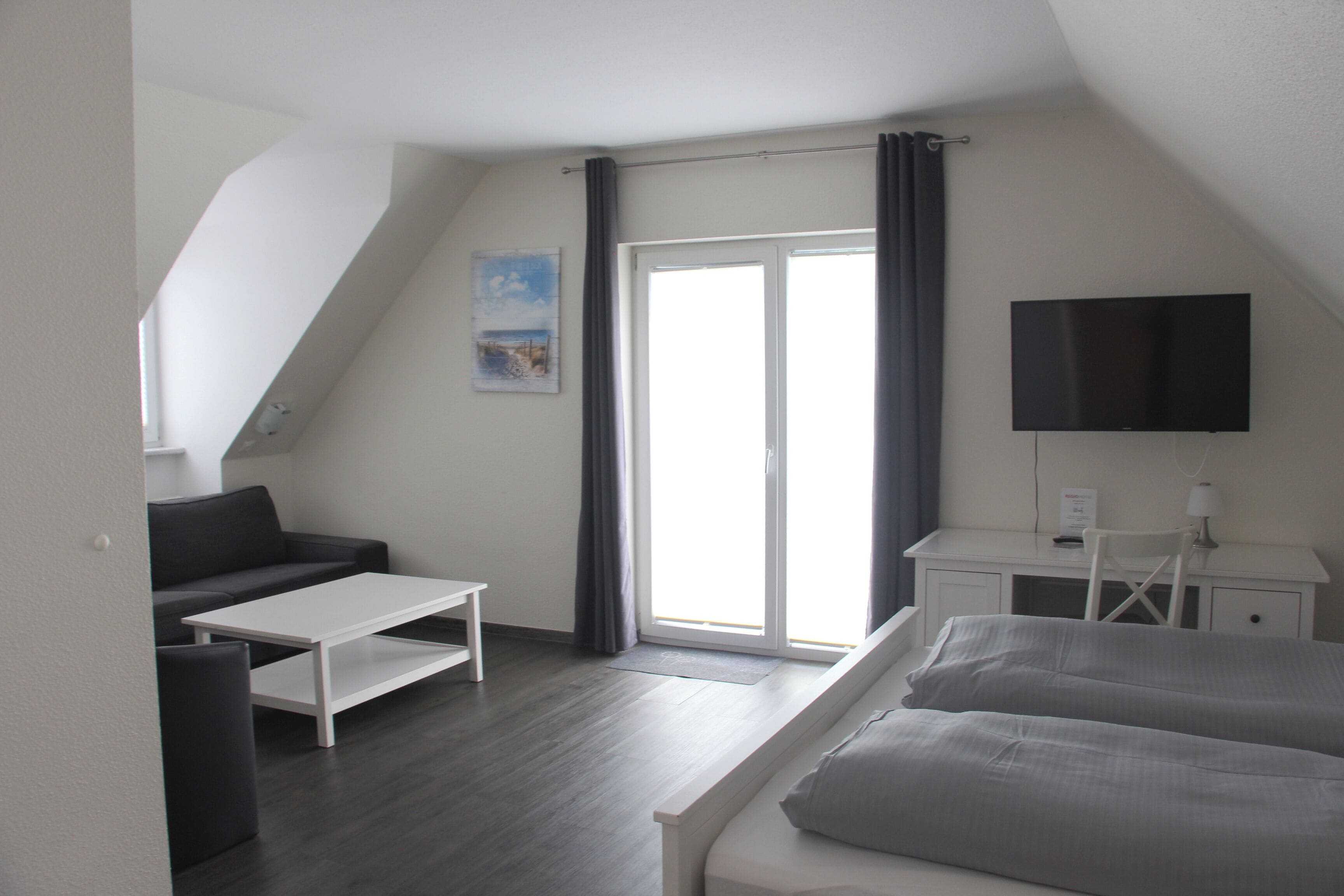 A modern hotel room with a bed, a sofa, a desk, and a TV.