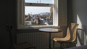 Une pièce dotée d’une grande fenêtre donnant sur un paysage urbain, de deux fauteuils en osier et d’une petite table ronde.