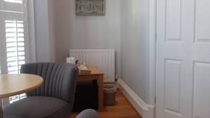 Un couloir avec un fauteuil gris, une petite table ronde, un radiateur et une porte blanche.