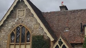 A stone building with a gabled roof, a large arched window, and a door with a coat of arms. - The Belfry at Yarcombe (Honiton)