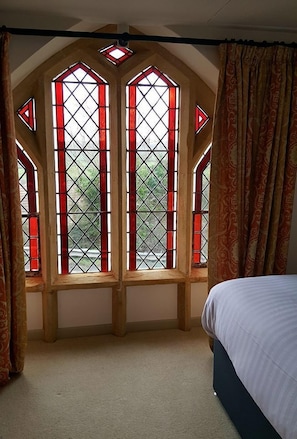 A bedroom with a bed, a window with stained glass, and curtains. - The Belfry at Yarcombe (Honiton)