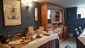 A dining area with a wooden table set for a meal, a vintage toaster, and a cabinet with glass doors. - The Belfry at Yarcombe (Honiton)