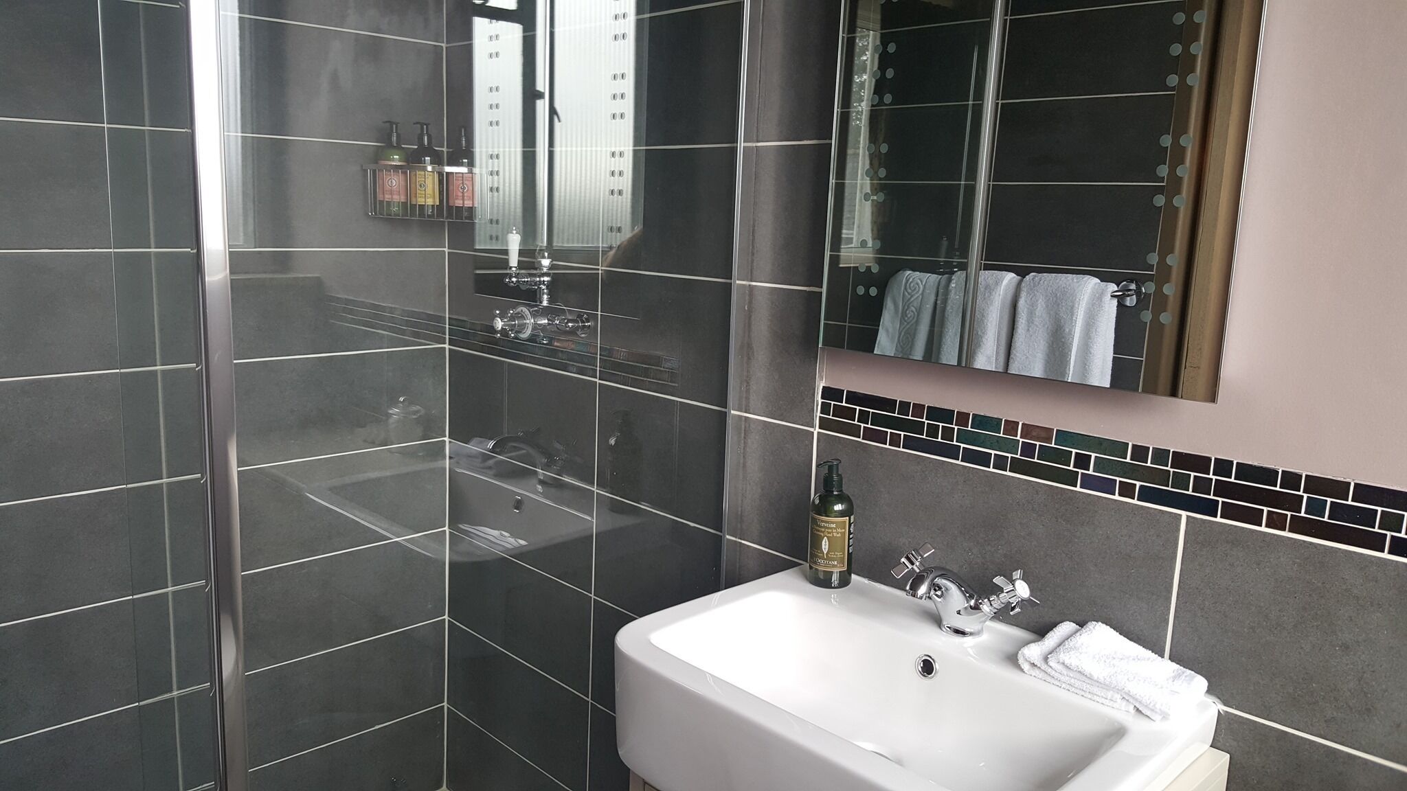 A modern bathroom with a large mirror, a white sink, and a shower area.