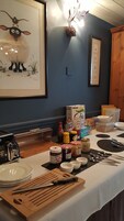 Una mesa de desayuno con diversos alimentos y utensilios, un cuadro en la pared y una cámara antigua a la izquierda.