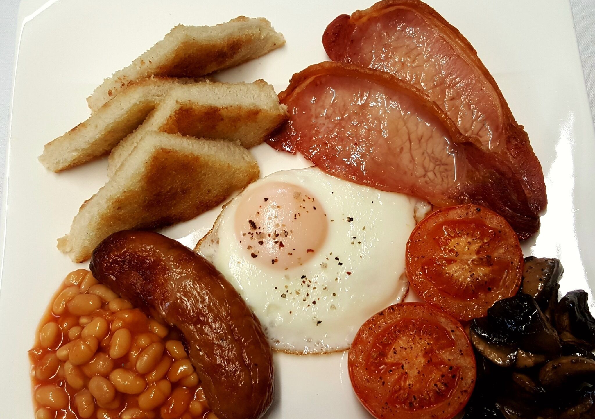 A plate of breakfast food including sausages, eggs, tomatoes, mushrooms, beans, and toast.