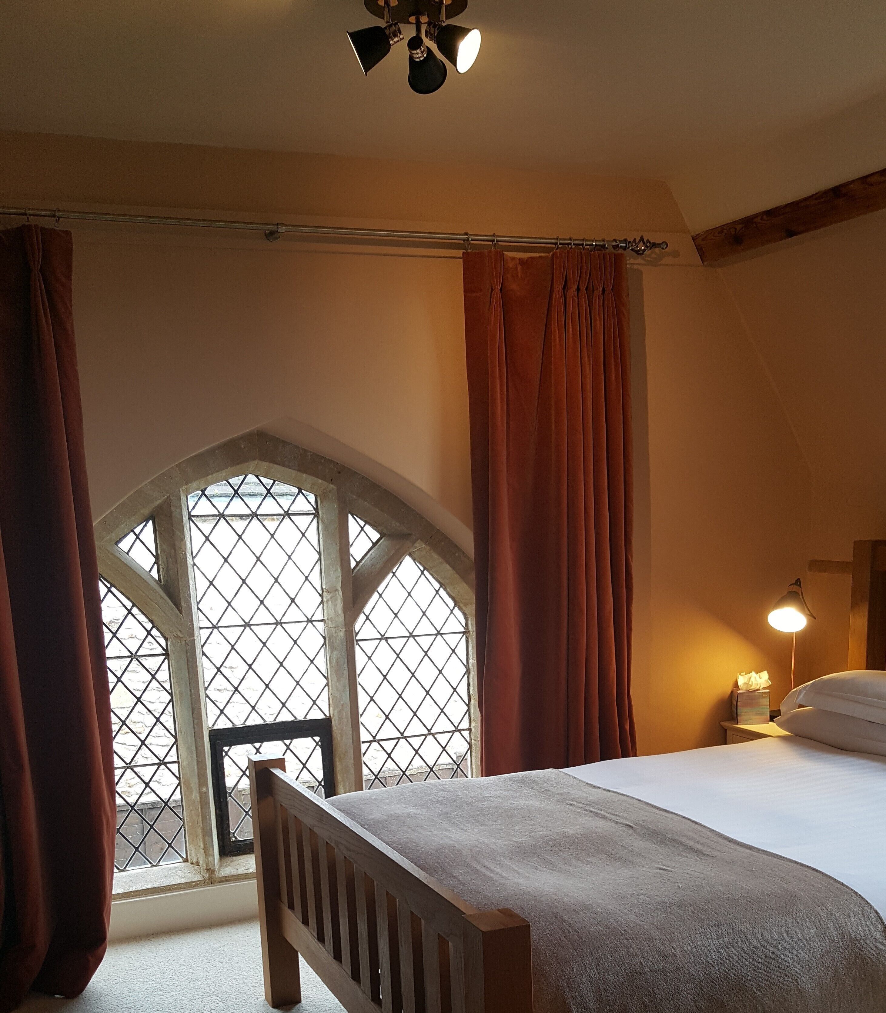 Ein Schlafzimmer mit einem großen Bett, einem Holz-Kopfteil, einem Nachttisch mit Lampe und einem Fenster mit Vorhängen.