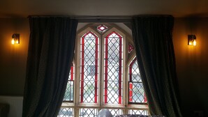 A room with a large stained glass window, two wall-mounted lights, and heavy drapes. - The Belfry at Yarcombe (Honiton)