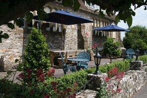 An outdoor seating area with stone walls, wooden benches, and blue umbrellas. - The Belfry at Yarcombe (Honiton)