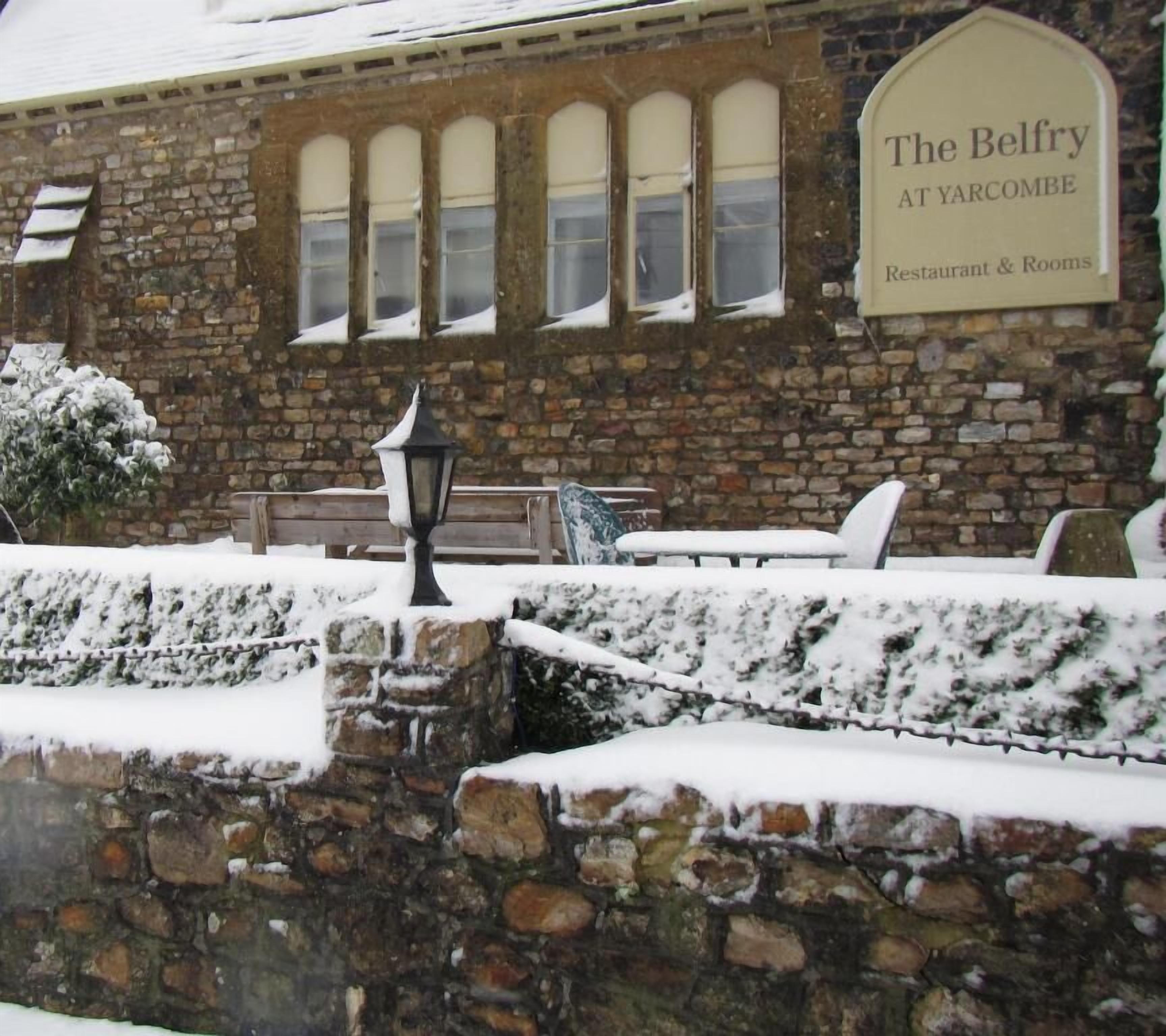 A stone building with a sign reading "The Belfry at Yarcombe Restaurant & Rooms".