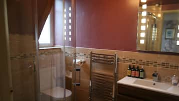 A bathroom with a glass shower enclosure, a toilet, a towel rack, and a sink with toiletries.