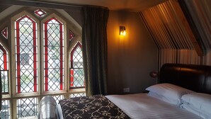 A hotel room with a bed, a window with stained glass, and a wall-mounted light. - The Belfry at Yarcombe (Honiton)