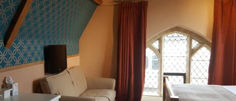 A room with a patterned wall, a window with a diamond lattice, a bed, and a television on a stand.