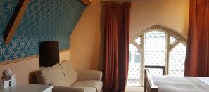 A room with a patterned wall, a window with a diamond lattice, a bed, and a television on a stand. - The Belfry at Yarcombe (Honiton)