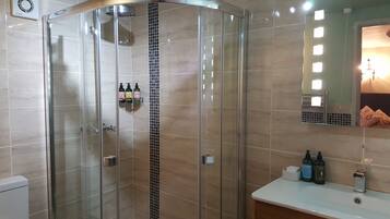 Une salle de bain moderne avec une douche à parois de verre, un meuble-lavabo avec un miroir et des articles de toilette.