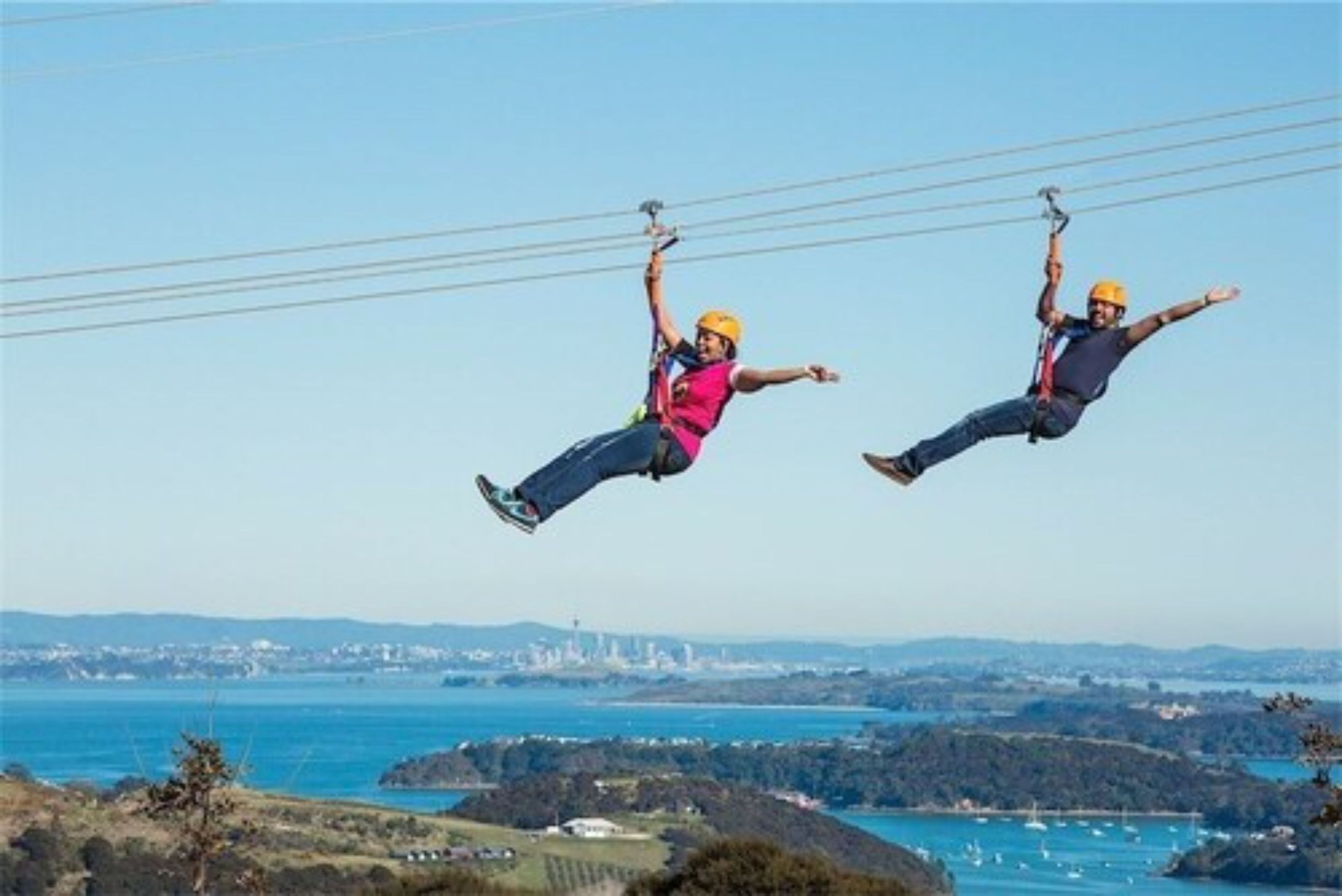 Två personer som hoppar bungyjump med en kustlandskap i bakgrunden.