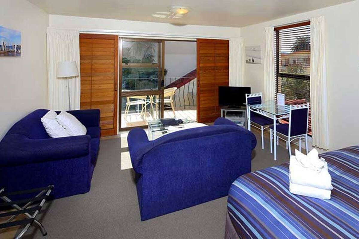 A hotel room with a bed, two sofas, a desk, a TV, and a balcony with a view.