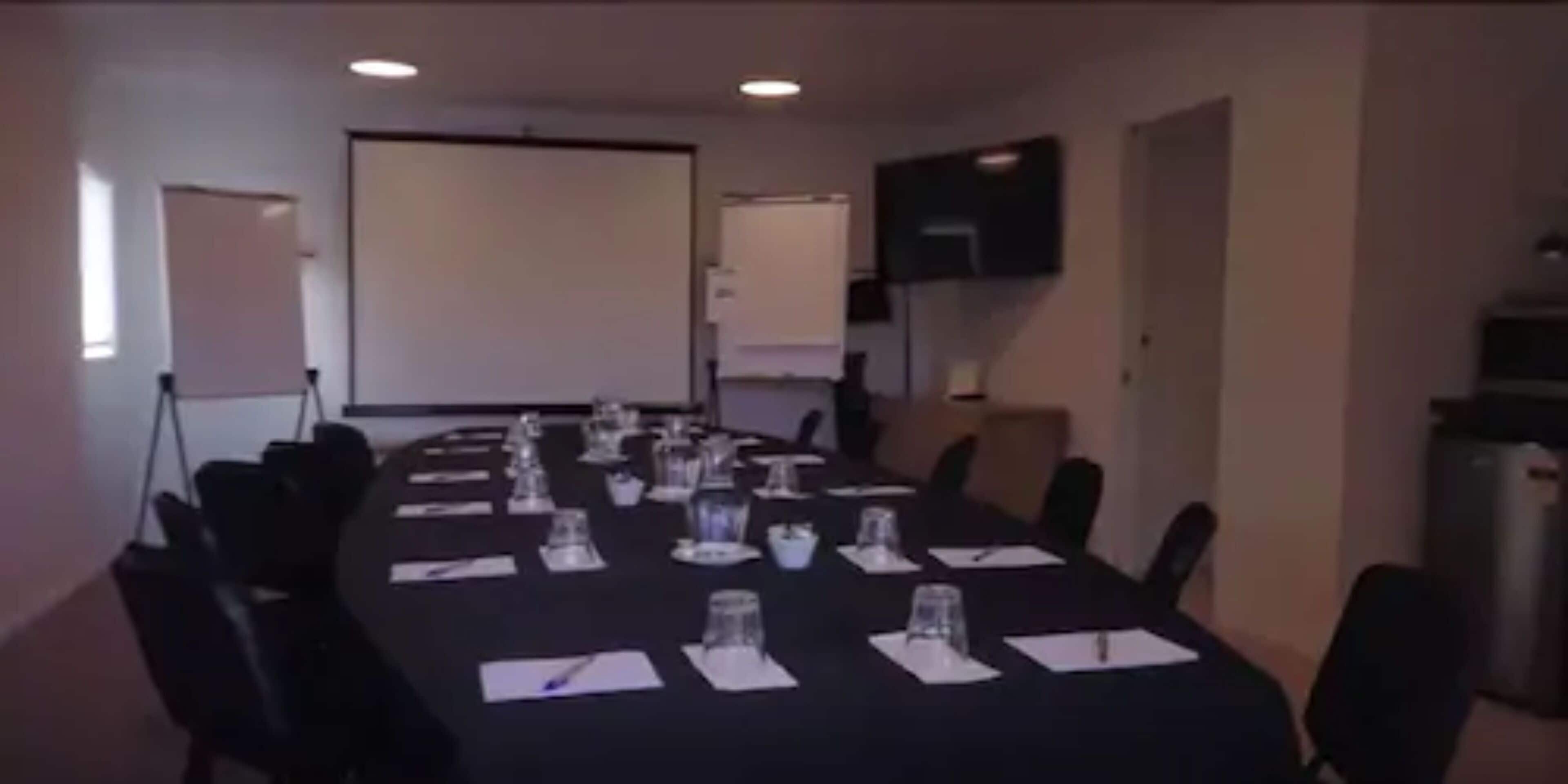 A conference room with a long table set for meetings, equipped with chairs, water glasses, and notepads.